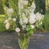 Tall white floral arrangement in a clear glass vase outdoors