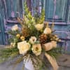 Cream roses and white blooms arranged in a white vase with pinecones
