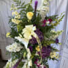 Standing floral spray with white, purple, and yellow blooms and a cream ribbon