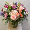 Mixed bouquet of pink roses, hydrangea, and purple daisies in a glass vase