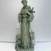 Green religious statue of a saint with a cross and two animals at the base