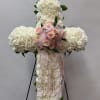 White floral cross with pink roses and ribbon on a stand