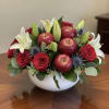 Red roses and white lilies arranged with apples in a white bowl.