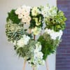 Heart-shaped floral wreath on a wooden easel with white and green flowers