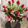 Red roses and pink lilies arranged in a glass vase with a striped ribbon.