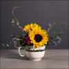Compact arrangement of sunflowers, purple thistles, and red blooms in a white skyline mug