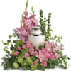 Pink flowers arranged around a white urn with silver trim