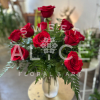 Arrangement of red roses in a clear glass vase with ferns on a small round table.