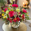 Round arrangement of bright pink and green carnations with yellow and red blooms in a clear glass vase