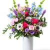 Tall mixed bouquet of pink roses, white anemones, and purple and blue blooms in a white vase
