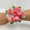 Pink rose wrist corsage with white ribbon accents and crystal bead sprays on a person's arm