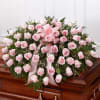 Large spray of light pink roses with ribbon displayed on a wooden casket.