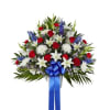 Fan-shaped red, white, and blue arrangement with roses, lilies, mums, and a blue ribbon in a white urn.