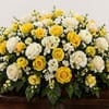 A broad, low casket spray of warm yellow and white roses that