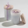 Pair of white glass jar candles with wooden lids, one lit and one tied with a lavender ribbon