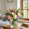 This enchanting floral arrangement blends soft peach hues with delicate greens and