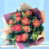 Bouquet of orange and red roses wrapped in peach and burgundy paper against a light blue background