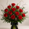 A dense cluster of velvety red roses rises from a clear glass
