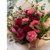 Hand-tied bouquet of red roses and mixed pink flowers wrapped in pale paper