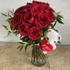 Red roses in a glass vase with a small white teddy bear