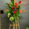 Tall tropical floral arrangement with red anthuriums and roses on a bamboo stand