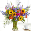 Mixed bouquet with sunflowers, purple irises, and orange roses in a glass vase