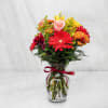 Mixed bouquet of red, pink, and yellow flowers in a glass vase with a ribbon