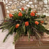 Bright clusters of orange roses form a warm, dignified casket spray designed