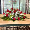Low floral centerpiece with red roses, white filler flowers, and greenery