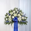 White lilies and blue flowers arranged with a large blue ribbon