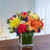 Colorful bouquet with orange lilies, yellow daisies, and pink carnations in a glass vase