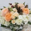 Low arrangement of peach and cream roses with white hydrangeas in a clear glass vase.