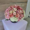Round arrangement of pink roses and white hydrangeas in a clear glass bowl vase on a pale cube stand