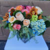 Low mixed arrangement of peach roses, blue hydrangeas and orchids in a square glass vase
