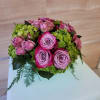 Low round arrangement of pink and lavender roses with green hydrangeas in a compact mound.