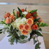Low arrangement of peach roses and tulips with white hydrangeas in a glass vase