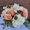 Low arrangement of peach roses, cream spray roses, and white hydrangeas in a round vase