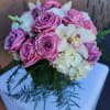 Round arrangement of pink roses, white hydrangeas, and orchids on a white pedestal