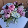 Low vase arrangement of pink and lavender roses, blue hydrangeas, and dark purple calla lilies.