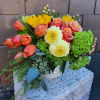 Low arrangement of orange tulips, yellow sunflowers, roses, mums and green hydrangea in a white vase