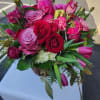 Round arrangement of red and pink roses and tulips in a rustic container