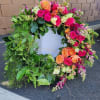 Large green wreath with bright pink and orange roses and accent flowers on one side
