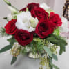 Low arrangement of red roses and white lisianthus with holiday greenery in a silver vase