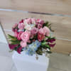 Rounded bouquet of pink roses, ranunculus, lilies and blue hydrangeas in a compact arrangement.