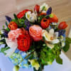 Compact arrangement of orange tulips, mixed roses, orchids, and blue and green hydrangeas.