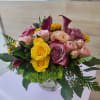 Round arrangement of yellow and pink roses with purple calla lilies in a clear glass vase