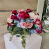 Low arrangement of pink roses, red ranunculus, blue hydrangeas, and dark pink calla lilies in a white vase