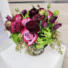 Compact bouquet of pink and burgundy roses with purple tulips and green hydrangeas in a glass vase