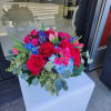 Round arrangement of red roses, pink blooms, blue hydrangea and purple flowers in a low vase