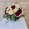 Low round arrangement of red and cream roses, blush spray roses, and white hydrangeas in a small bowl vase.